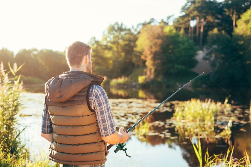 hombre de espaldas pescando en lago con nenufares desenfocados